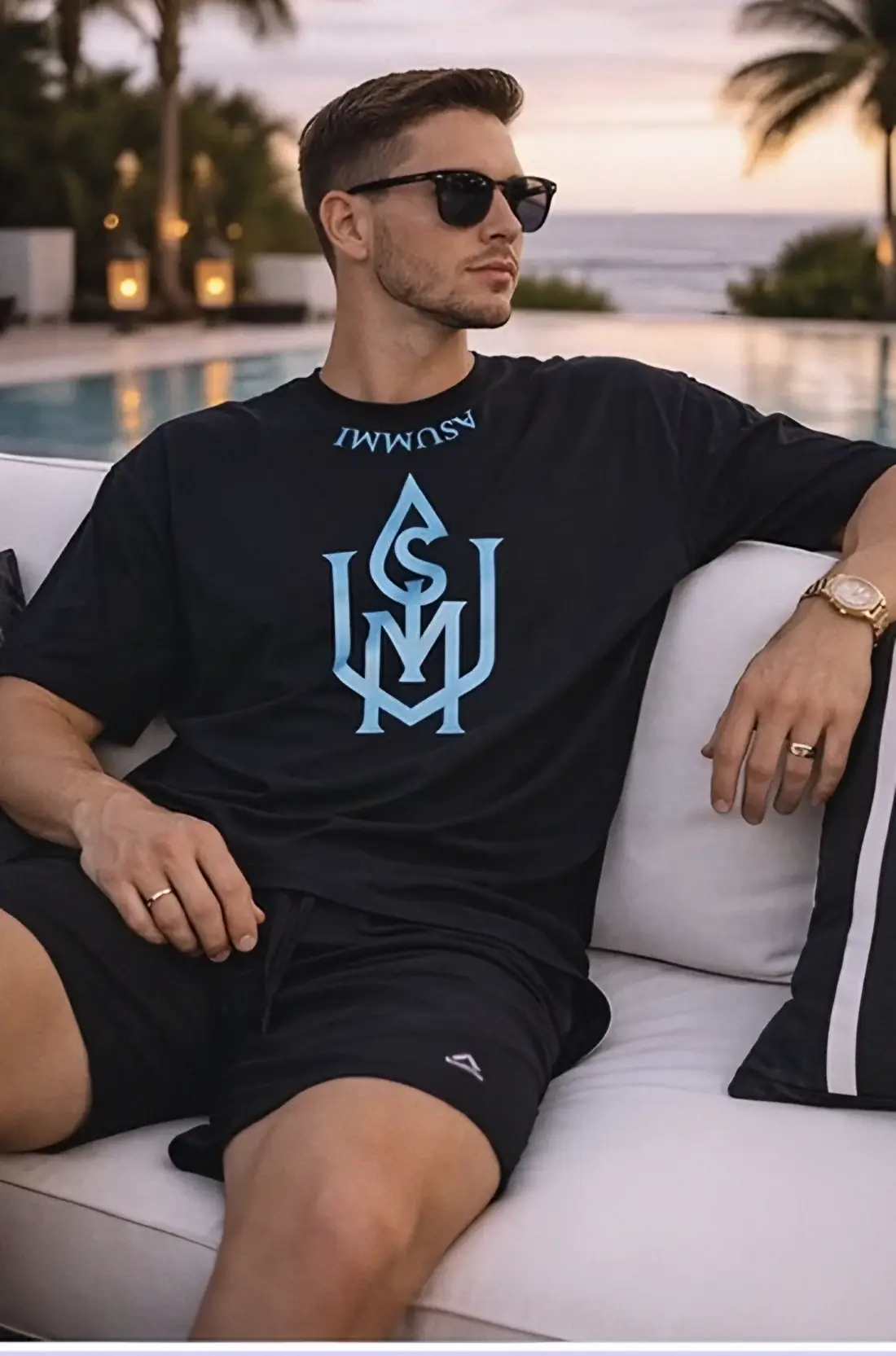 Man in a black ASUMMI monogram tee by a pool at sunset